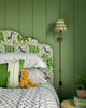 bed with La Jungle Green headboard, green painted wall behind with soprano green cushion on bed using pom parade trim. Lion soft toy next to cushion. Design by Kit & Co